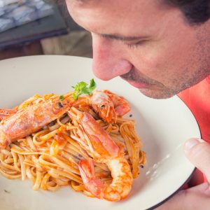 Men smelling plate of spaghetti with langostino